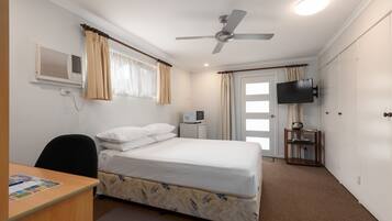 Hotelkamer met een enkel bed, een bureau, een stoel, een plafondventilator, een televisie en een raam met gordijnen.