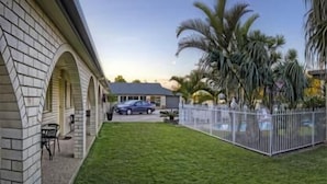 A house with a brick exterior, a well-maintained lawn, a parked car, and a white fence.
