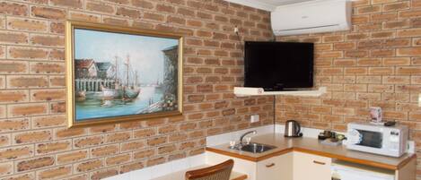 A compact kitchen with a brick wall, a painting, a television, and basic amenities.