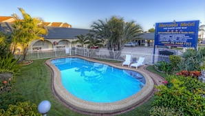 A swimming pool surrounded by a white fence, with a sign for Marcola Motel in the background.