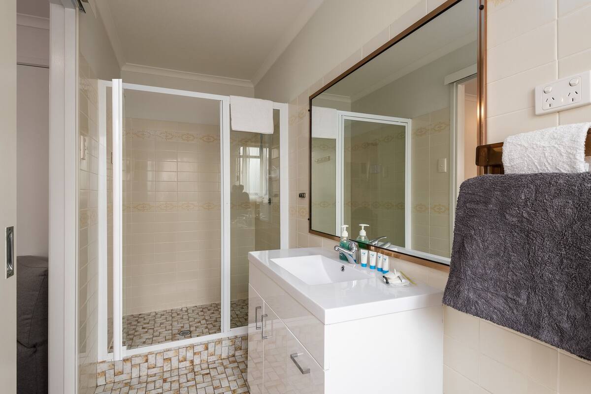 A bathroom with a glass shower enclosure, a white sink, and a large mirror.