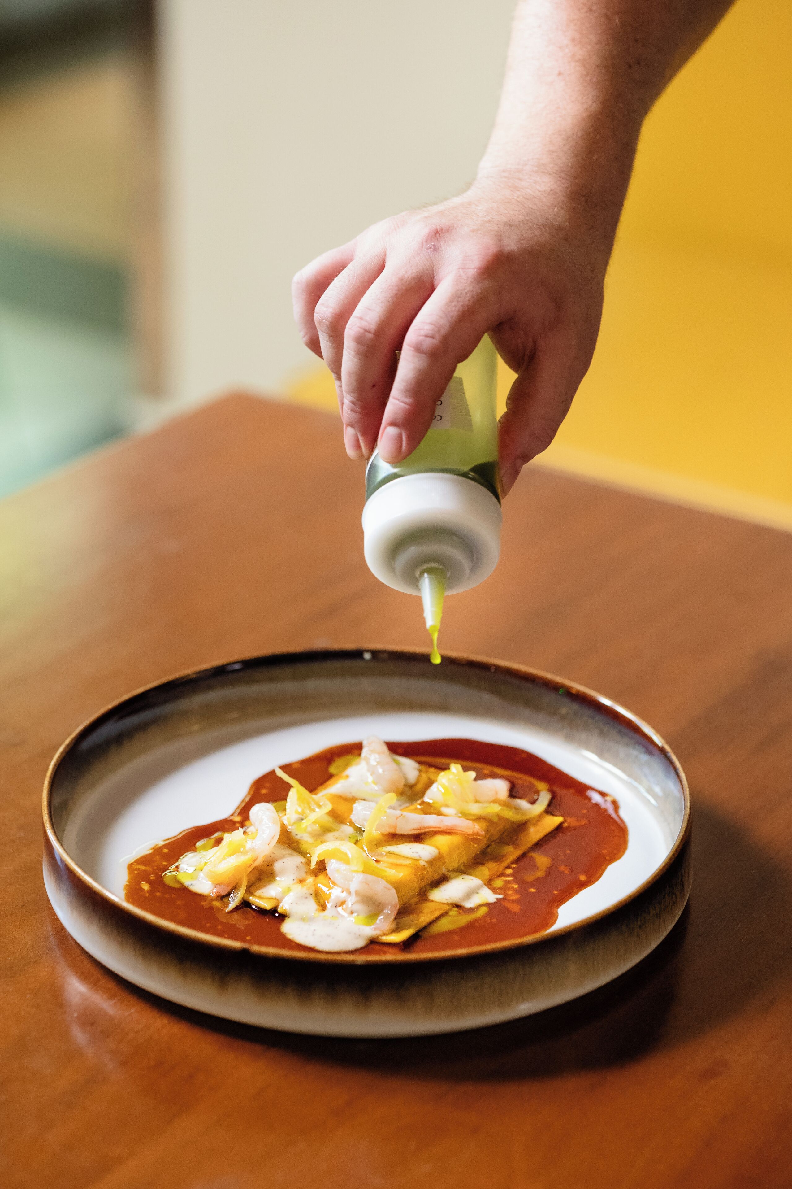 A hand pouring sauce onto a plate of food.