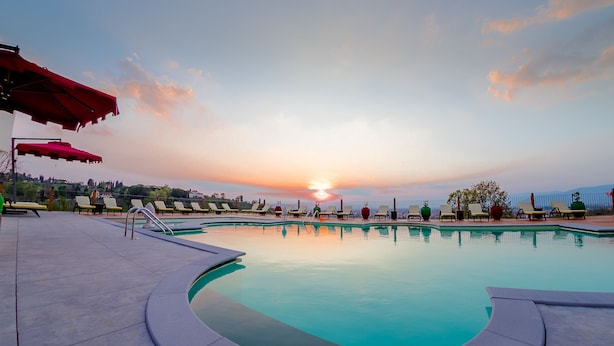 Une piscine bordée de chaises longues et d’ombrelles, le tout mis en valeur par le décor d’un coucher de soleil.