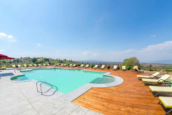 A pool with lounge chairs and a wooden deck, overlooking a cityscape. - Villa Tolomei Hotel & Resort (Florence)