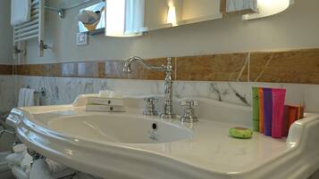 A bathroom with a large white sink, multiple faucets, and a mirror above. There are toiletries and a green soap dish on the sink.