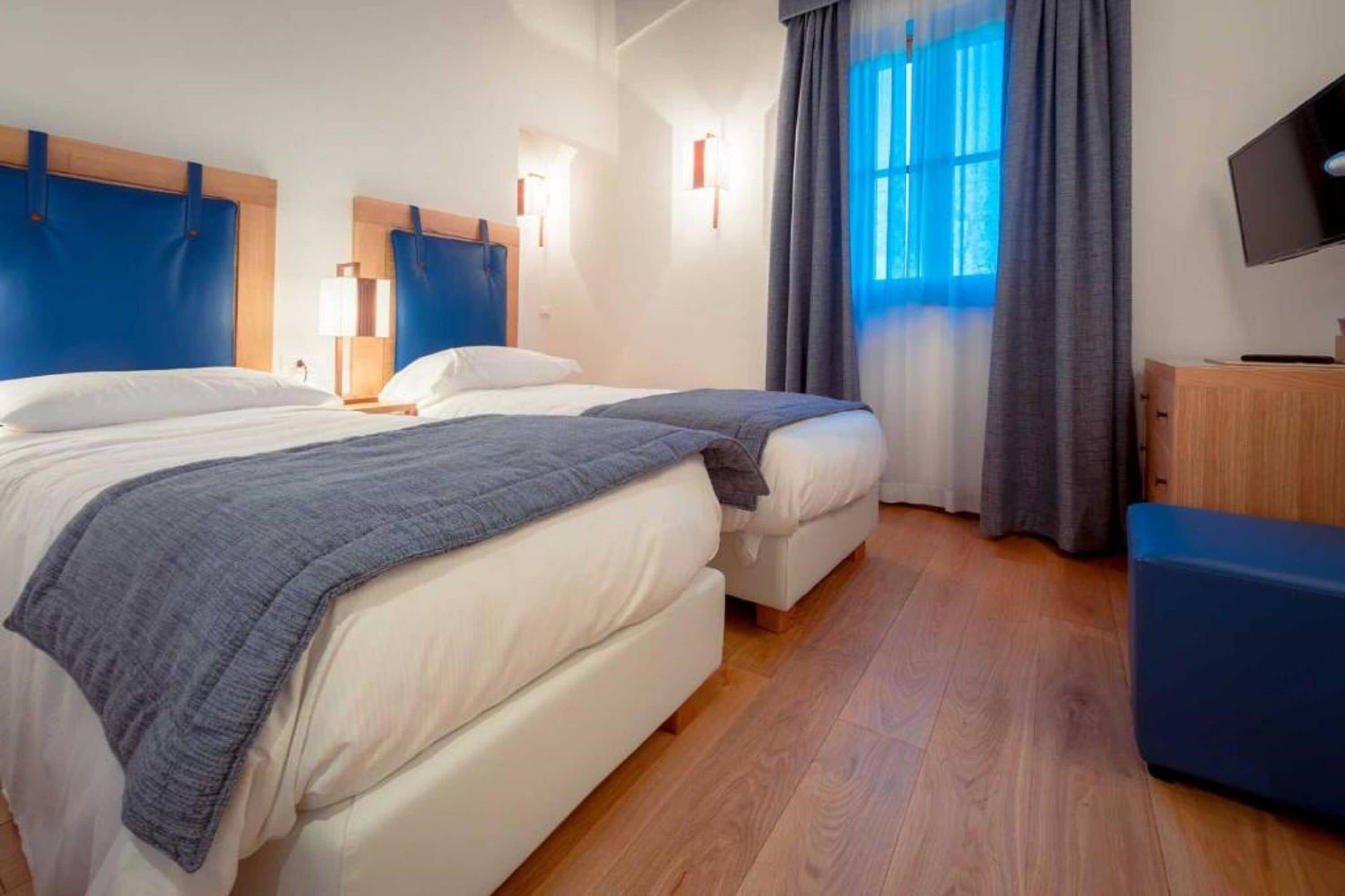 A hotel room with two beds, a TV, and a wooden floor.