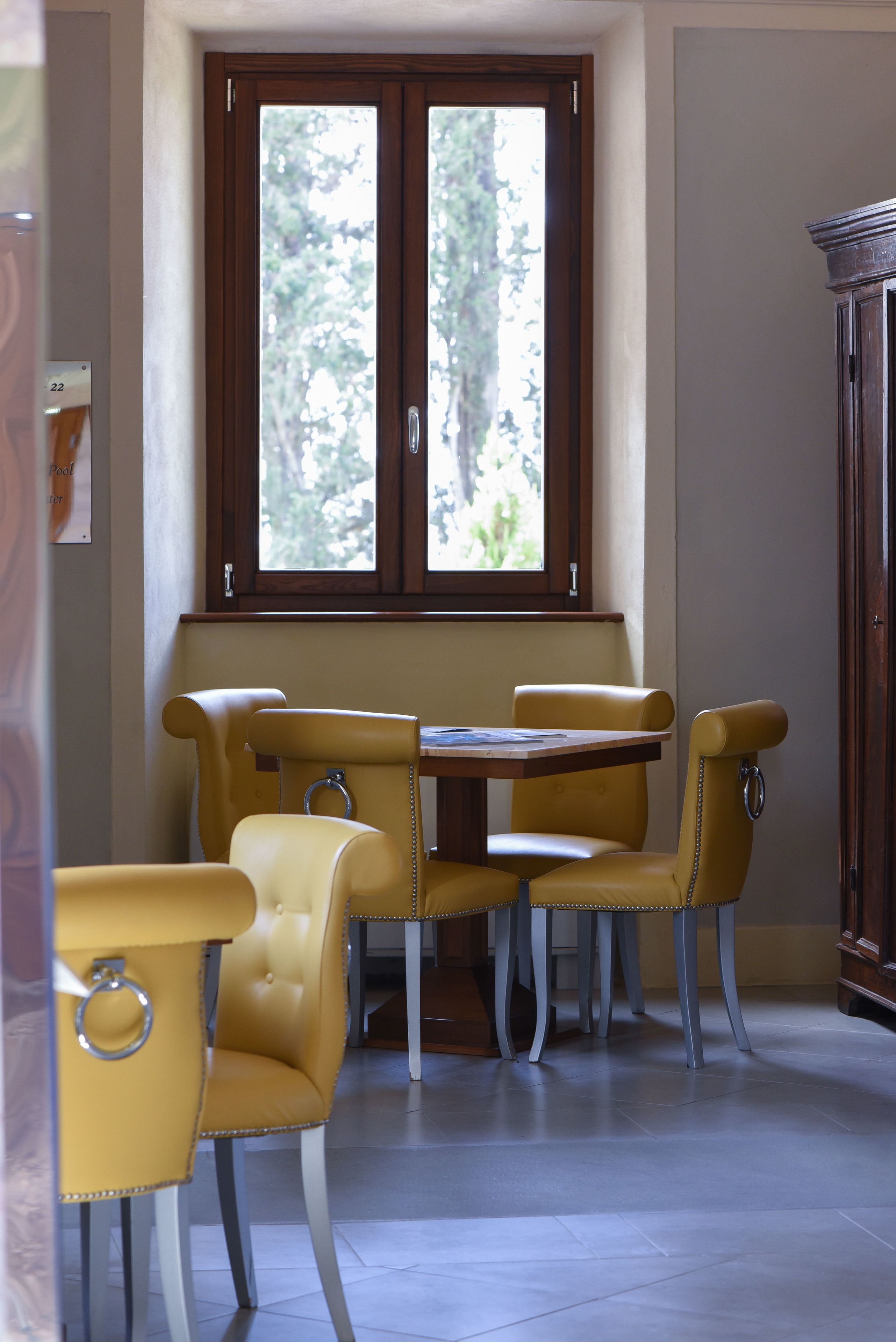 A dining area with a table and four chairs, a window with a view of trees, and a cabinet to the right.