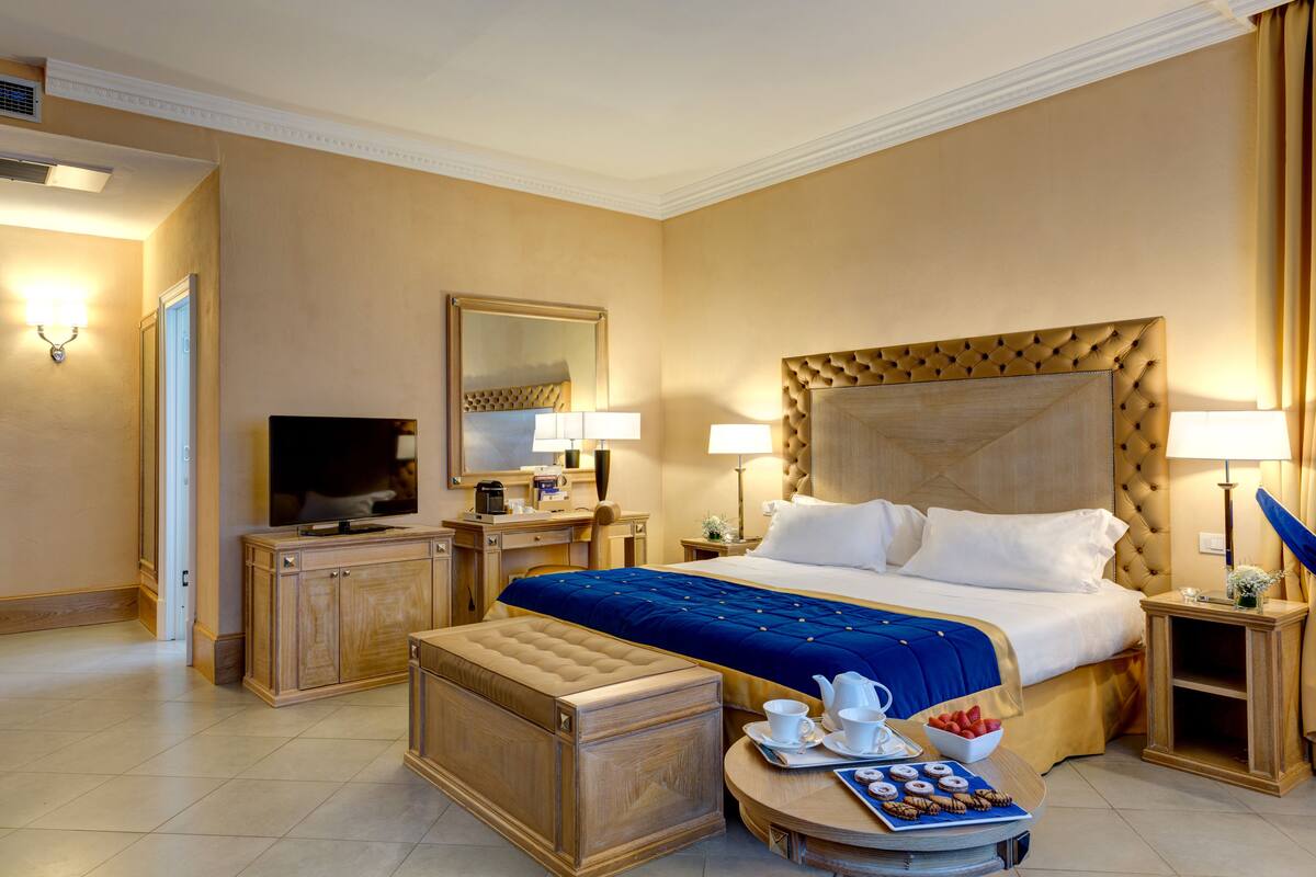 A hotel room with a large bed, a television, a desk, and a small table with a tray of pastries.