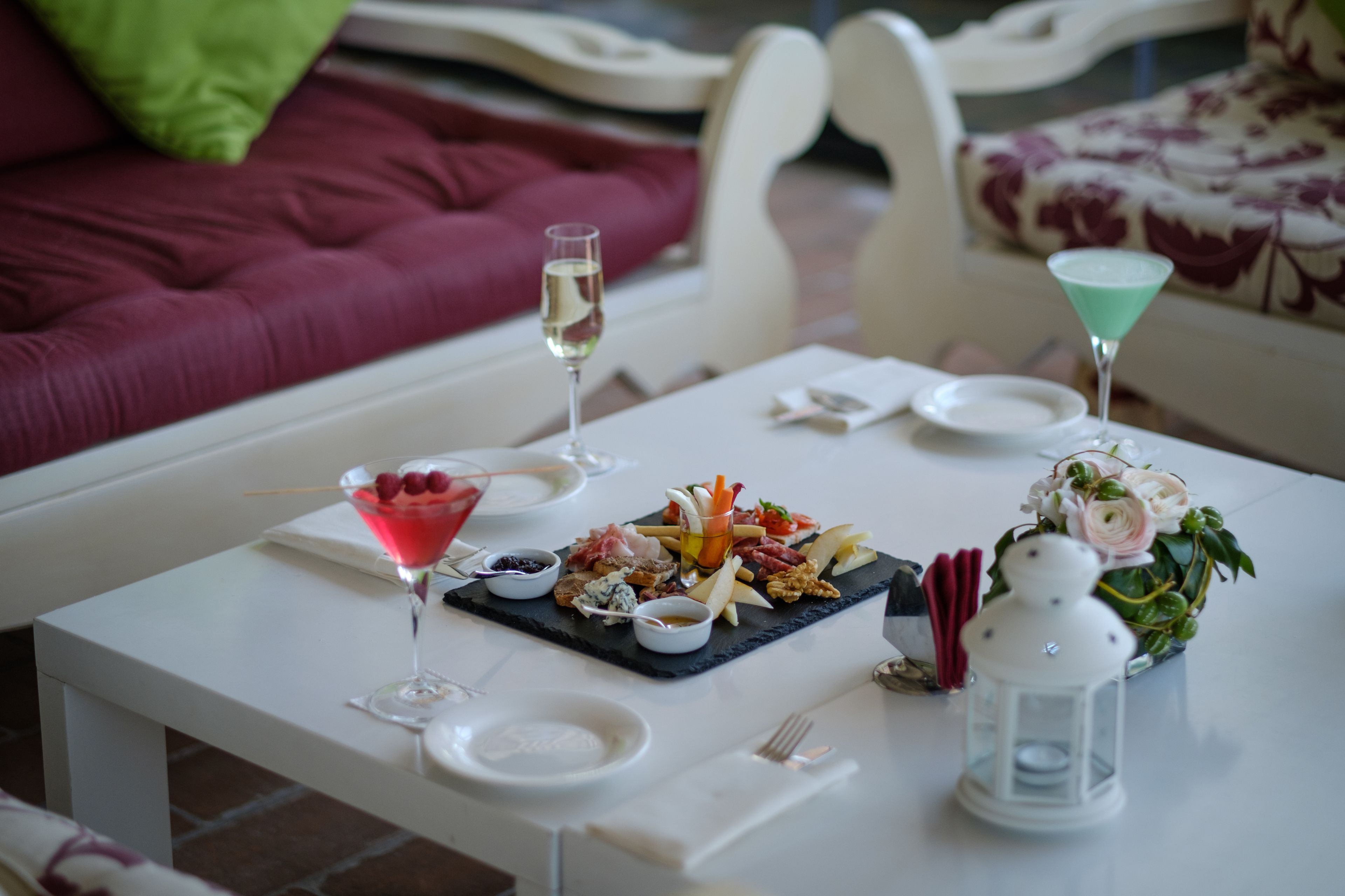 Una mesa de comedor con una variedad de comida y bebidas, incluyendo un martini, una tabla de quesos y una vela.