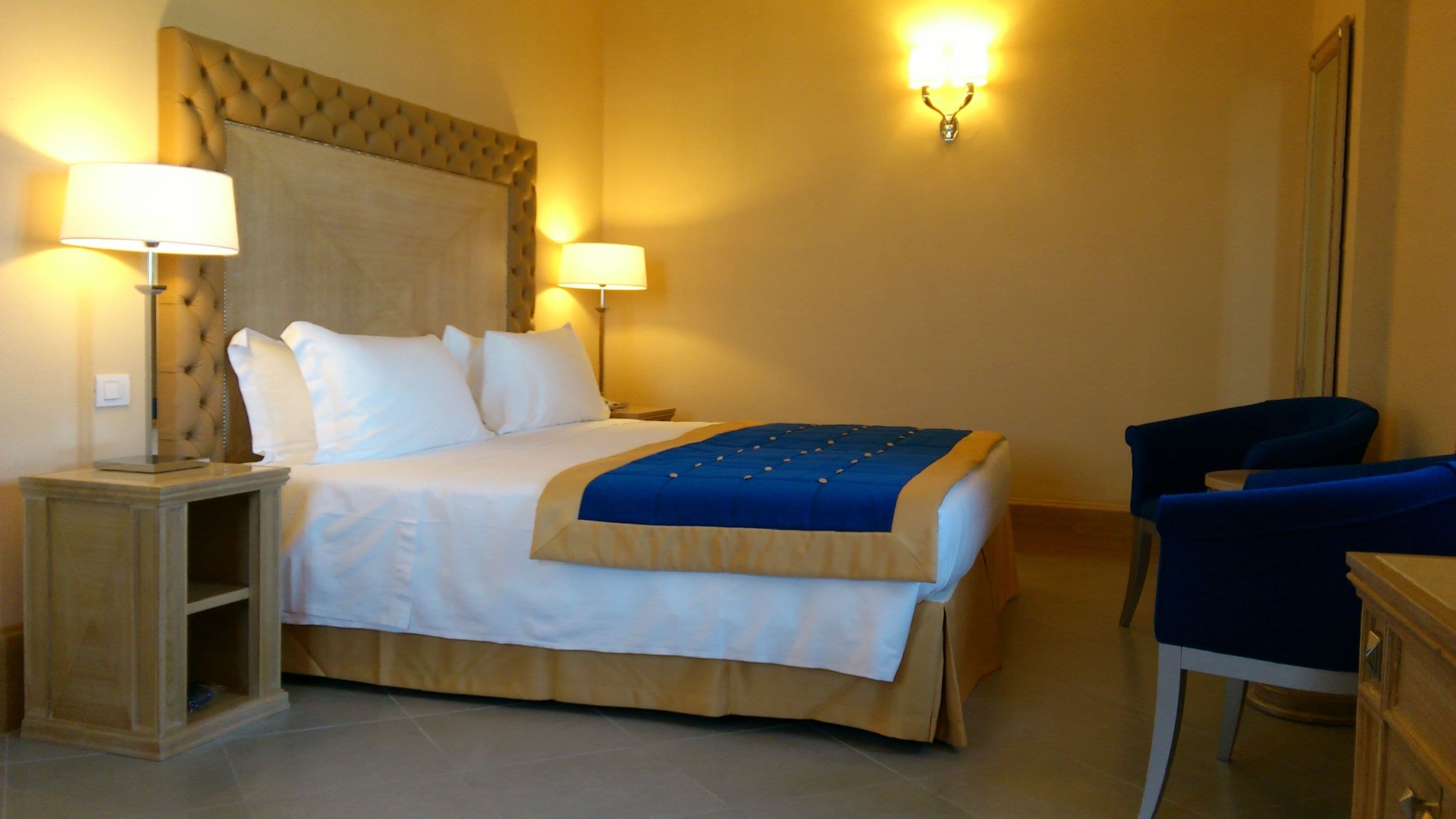 Una habitación de hotel con una cama, dos lámparas de noche, una silla y un aparador.
