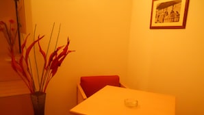 A dining area with a white table and red chair, a vase with red plants, and a framed picture on the wall. - Catania Crossing B&B Rooms and Comforts (Catania)