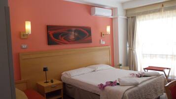 Quarto de hotel com cama, mesas de cabeceira, ar condicionado, um quadro na parede e uma janela com cortinas.