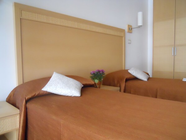 A hotel room with two beds, a nightstand, a lamp, and a wardrobe.
