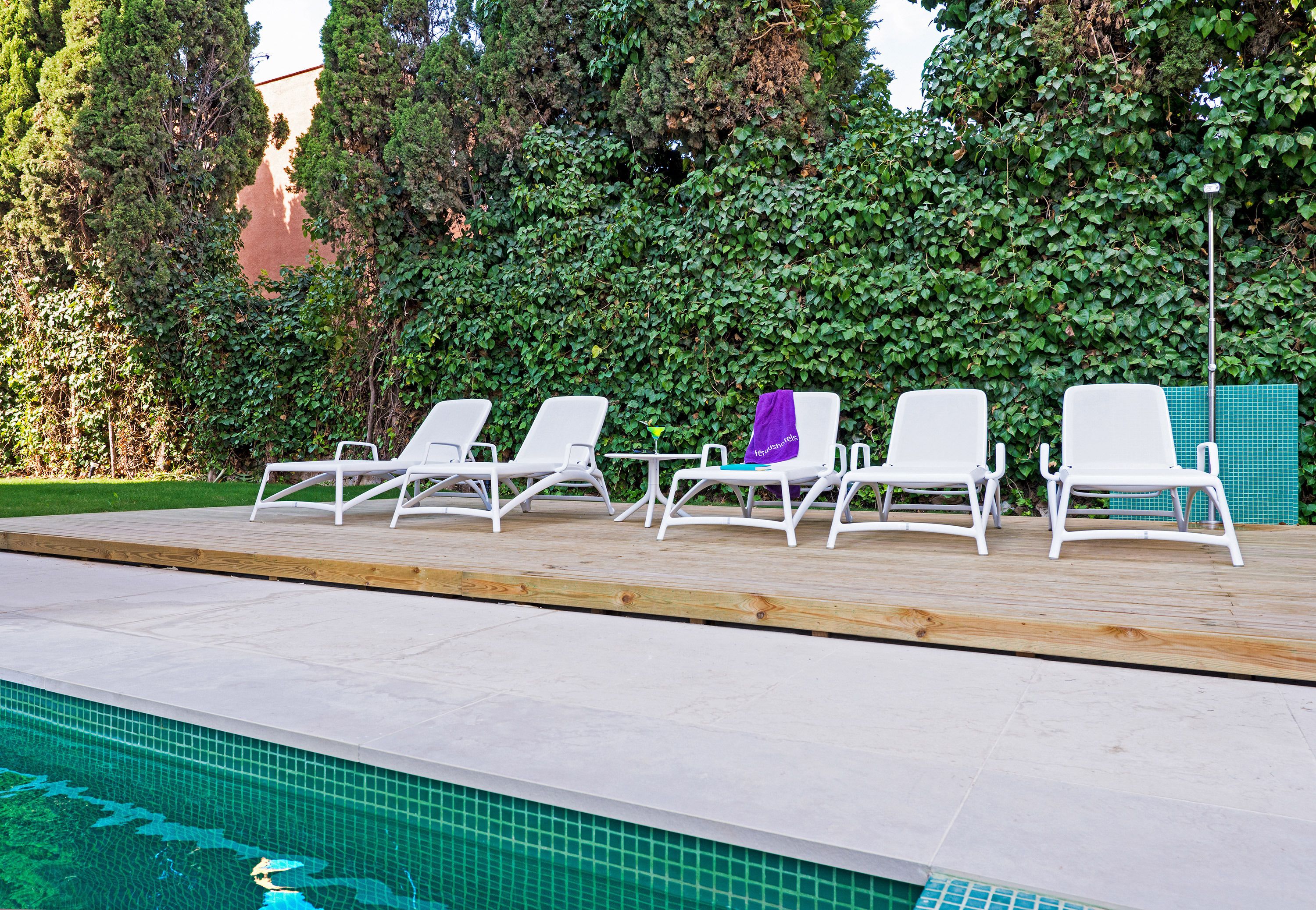 Una piscina con sillas de descanso blancas y un muelle de madera.