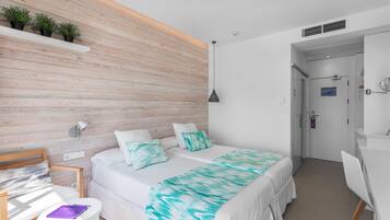 Un dormitorio moderno con una pared de acento de madera, una cama con colcha verde azulada y blanca, un escritorio con silla y una pequeña mesa con un cuaderno morado.