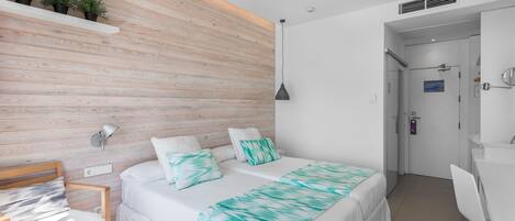 A modern bedroom with a wooden accent wall, a bed with a teal and white bedspread, a desk with a chair, and a small table with a purple notebook.