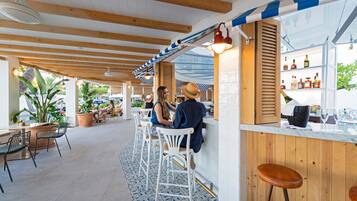 Una zona de bar con vigas de madera, taburetes blancos y suelo de baldosas.