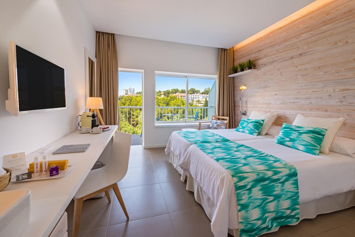 A modern hotel room with a large bed, a desk, a TV, and a balcony with a view of the city.