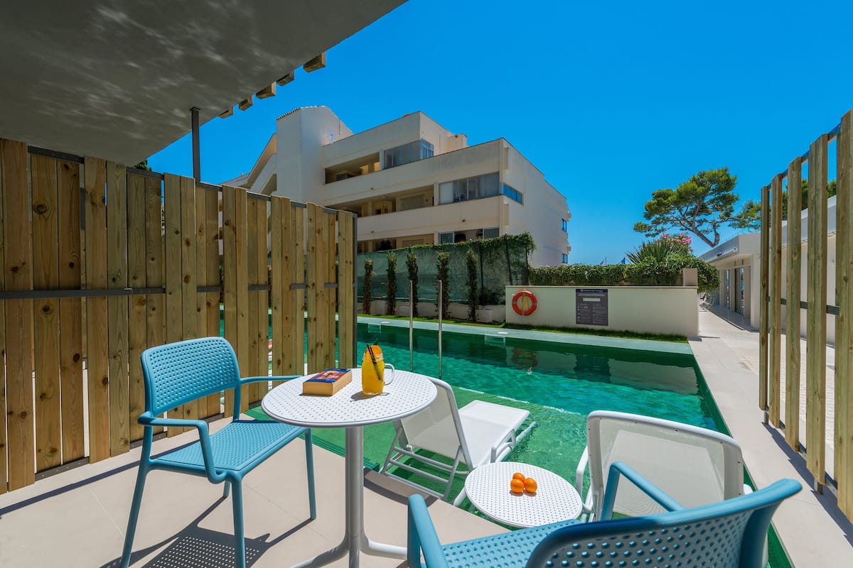 A poolside area with a wooden fence, a small table with a book and a bottle, and two blue chairs.