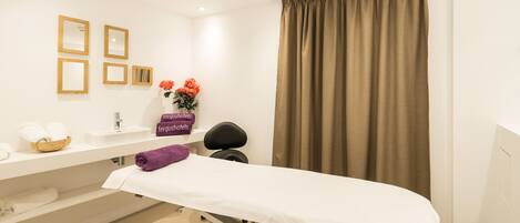 Un consultorio médico moderno y limpio, con una cama, una mesa de exploración y un lavabo con una cesta de toallas.