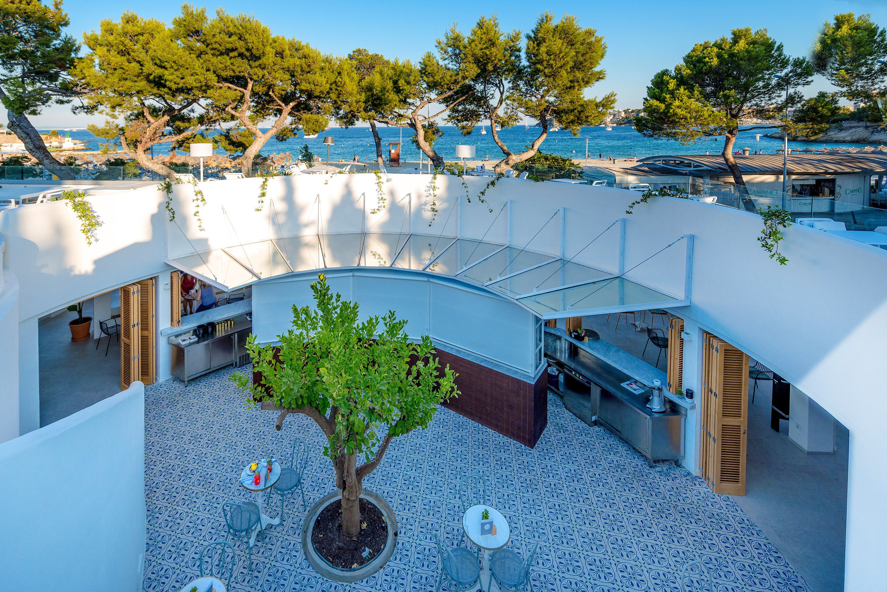 A rooftop terrace with a potted tree, outdoor seating, and a view of the sea.