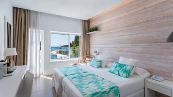 Una moderna camera d'albergo con un letto grande, una scrivania con una lampada e vista sul mare dalla finestra.
