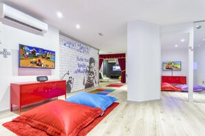 A modern hotel room with a large TV, a red cabinet, colorful pillows, and a wall with a motivational quote.