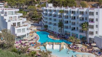 Ein Resort mit einem zentral gelegenen Schwimmbad, umgeben von Liegebereichen und Palmen.