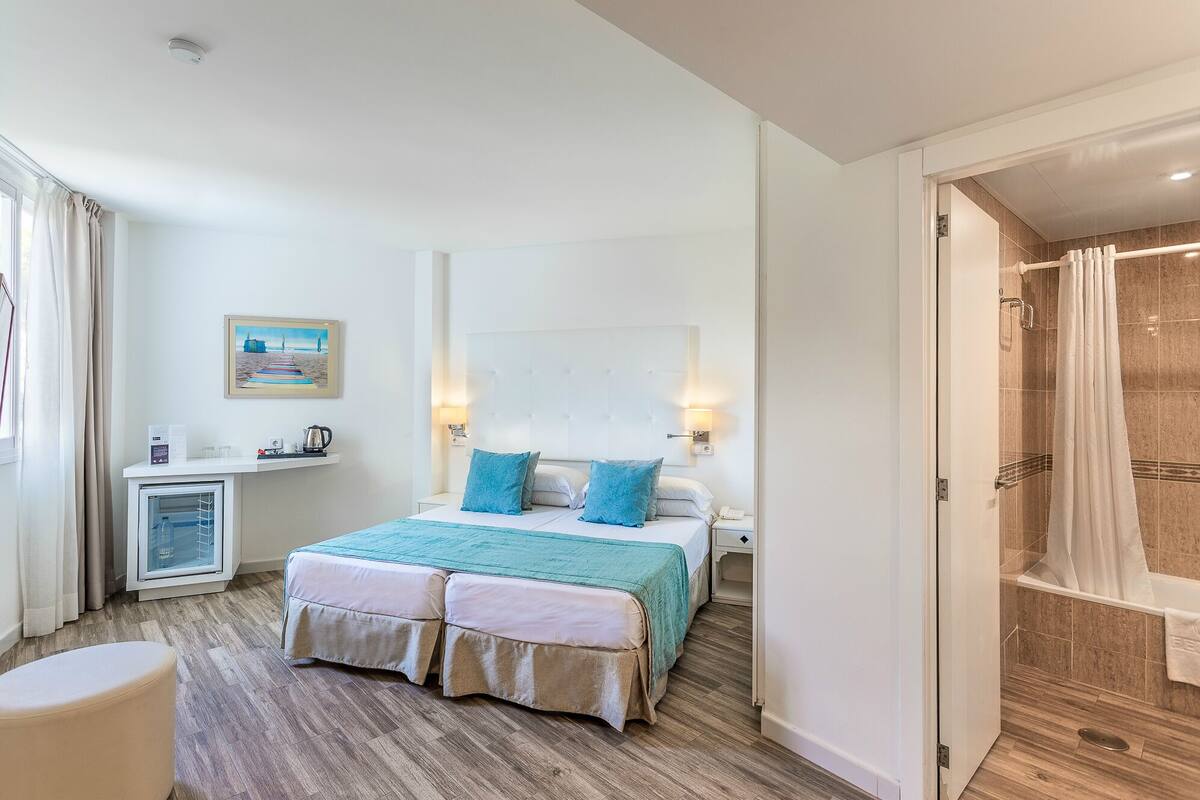A hotel room with a bed, bedside table, and a shower area.