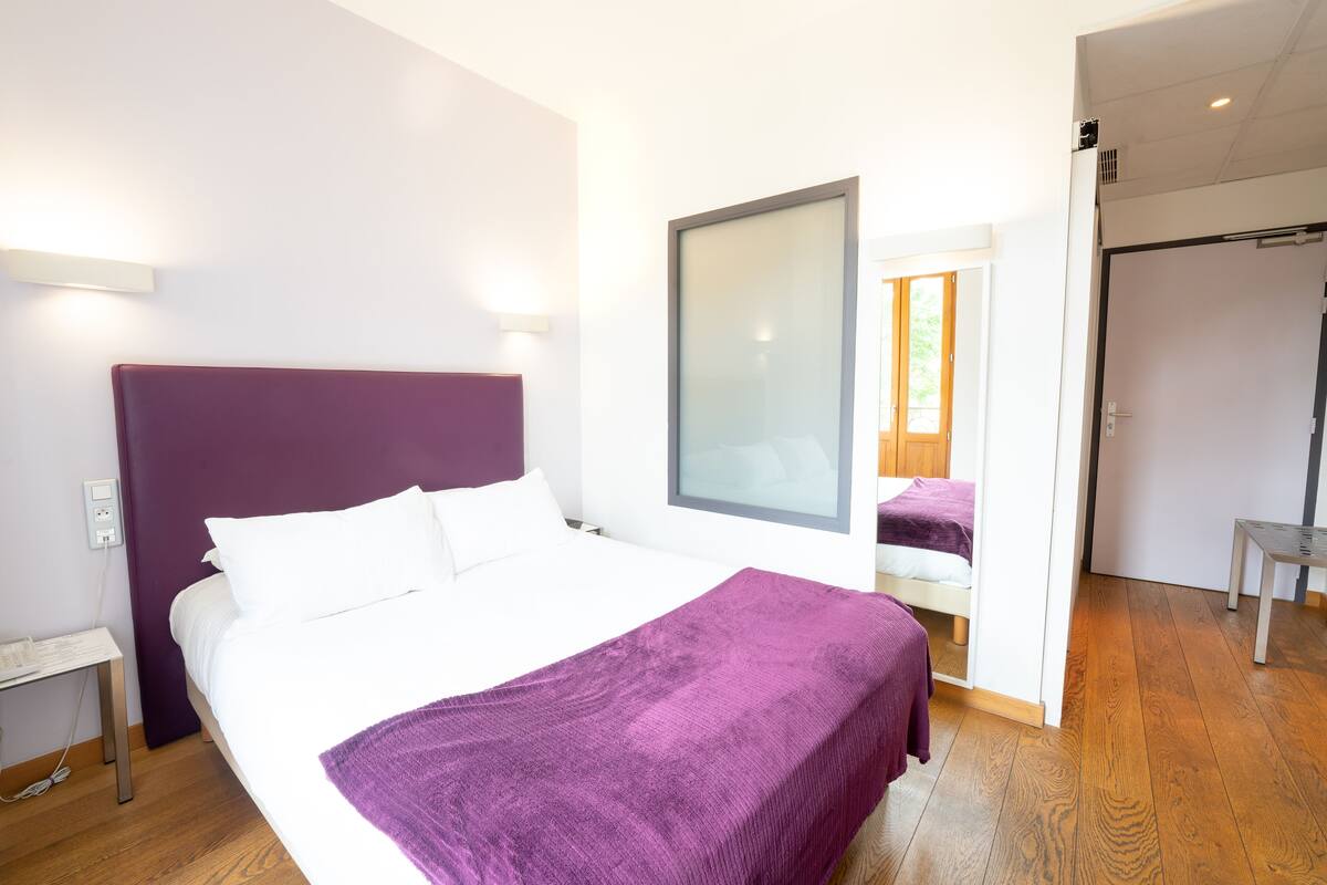 Ein modernes Hotelzimmer mit einem großen Bett, einem Nachttisch, einem Spiegel und Holzboden.