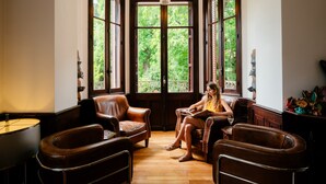 Una habitación con un amplio ventanal, sillones de cuero, suelo de madera y un candelabro.