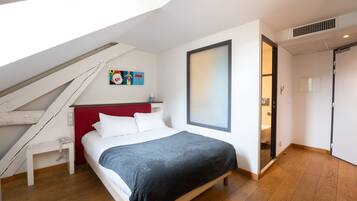 A bedroom with a bed, a red headboard, a white nightstand, a wooden floor, a skylight, and a painting on the wall.