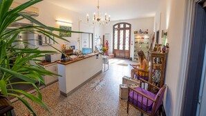 Un vestíbulo amplio con una recepción, una araña, una zona de estar con una silla morada y un espejo decorativo.
