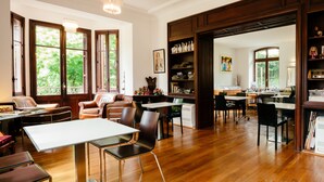Una habitación amplia con pisos de madera, ventanas grandes y diversas opciones de mobiliario, incluyendo mesas y sillas.