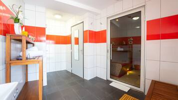 A modern bathroom with white and red tiles, a wooden bench, and a glass shower enclosure.