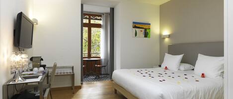 A hotel room with a bed, a desk, a chair, a television, and a window with a view of trees.