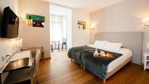 Habitación de hotel con cama, escritorio con silla, televisor, obras de arte en las paredes y bandeja de desayuno sobre la cama.