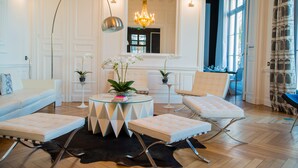 A modern living room with a sofa, two ottomans, a glass coffee table, and a chandelier. - Art Hôtel Rochecorbon (Rochecorbon)