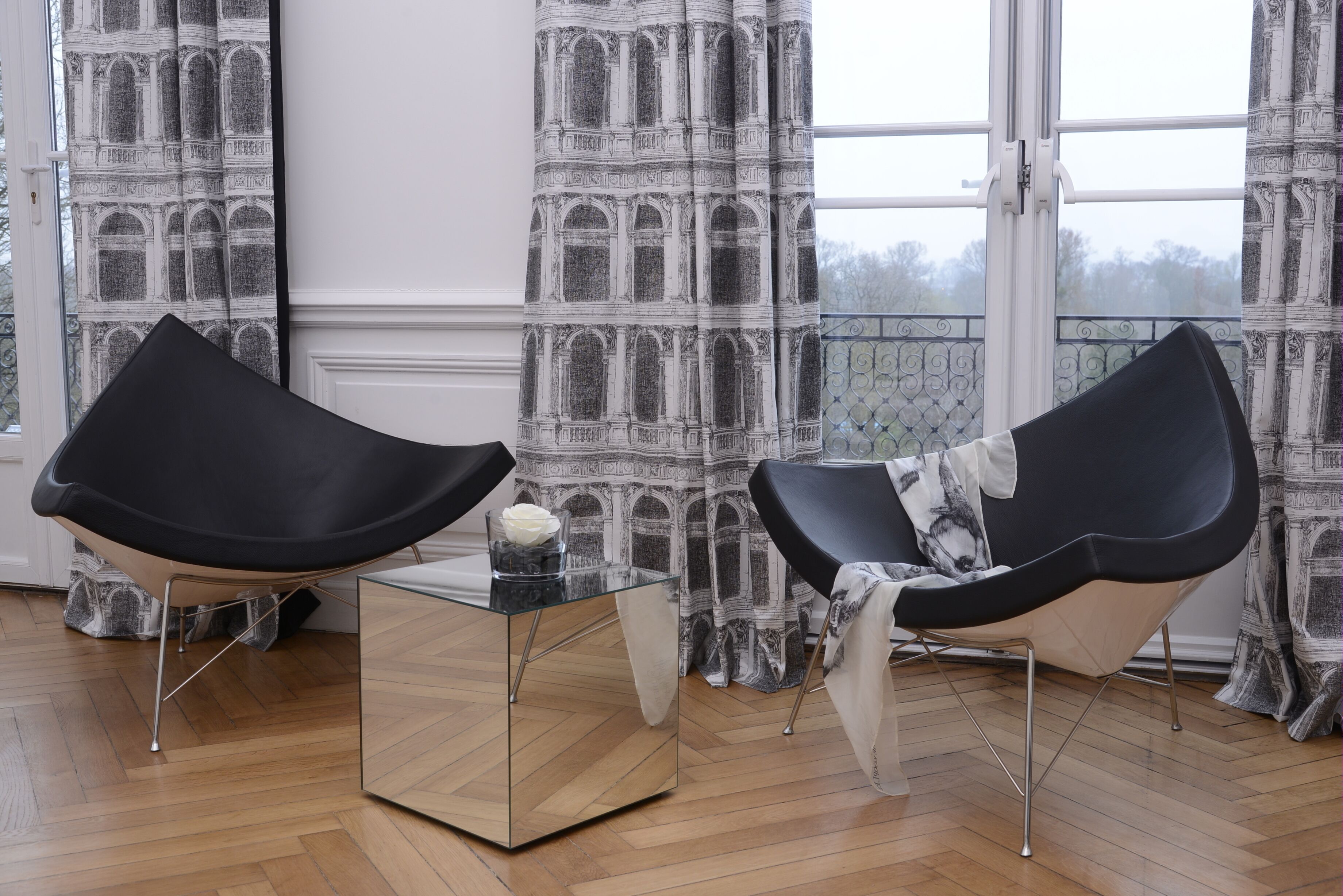 A room with two black chairs, a glass coffee table, and patterned curtains.