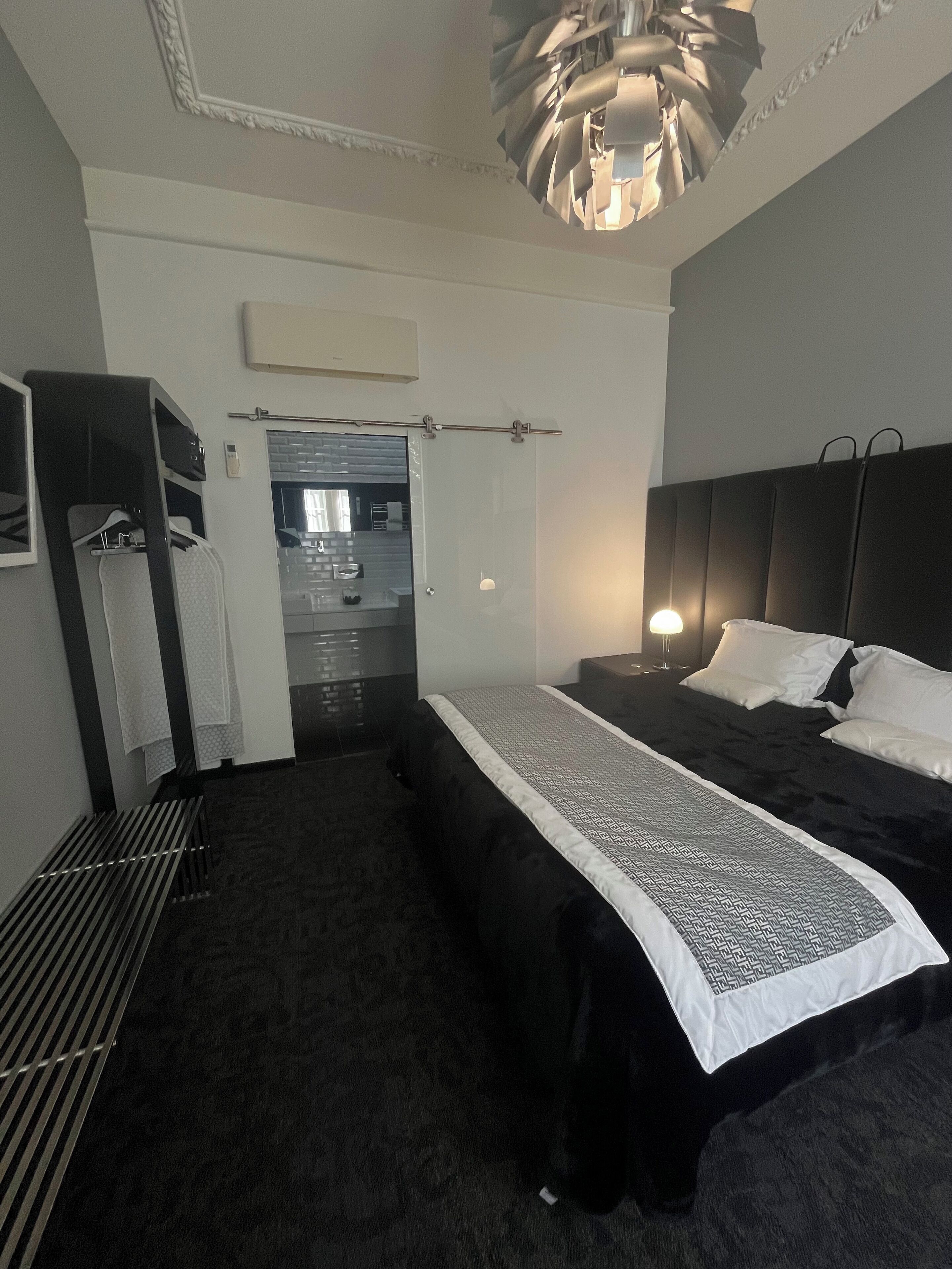 Hotelkamer met een groot bed, nachtkastje, kledingkast en een badkamer door een open deur zichtbaar.