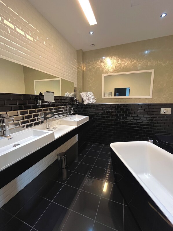 A modern bathroom with two sinks, a large mirror, and a freestanding bathtub.