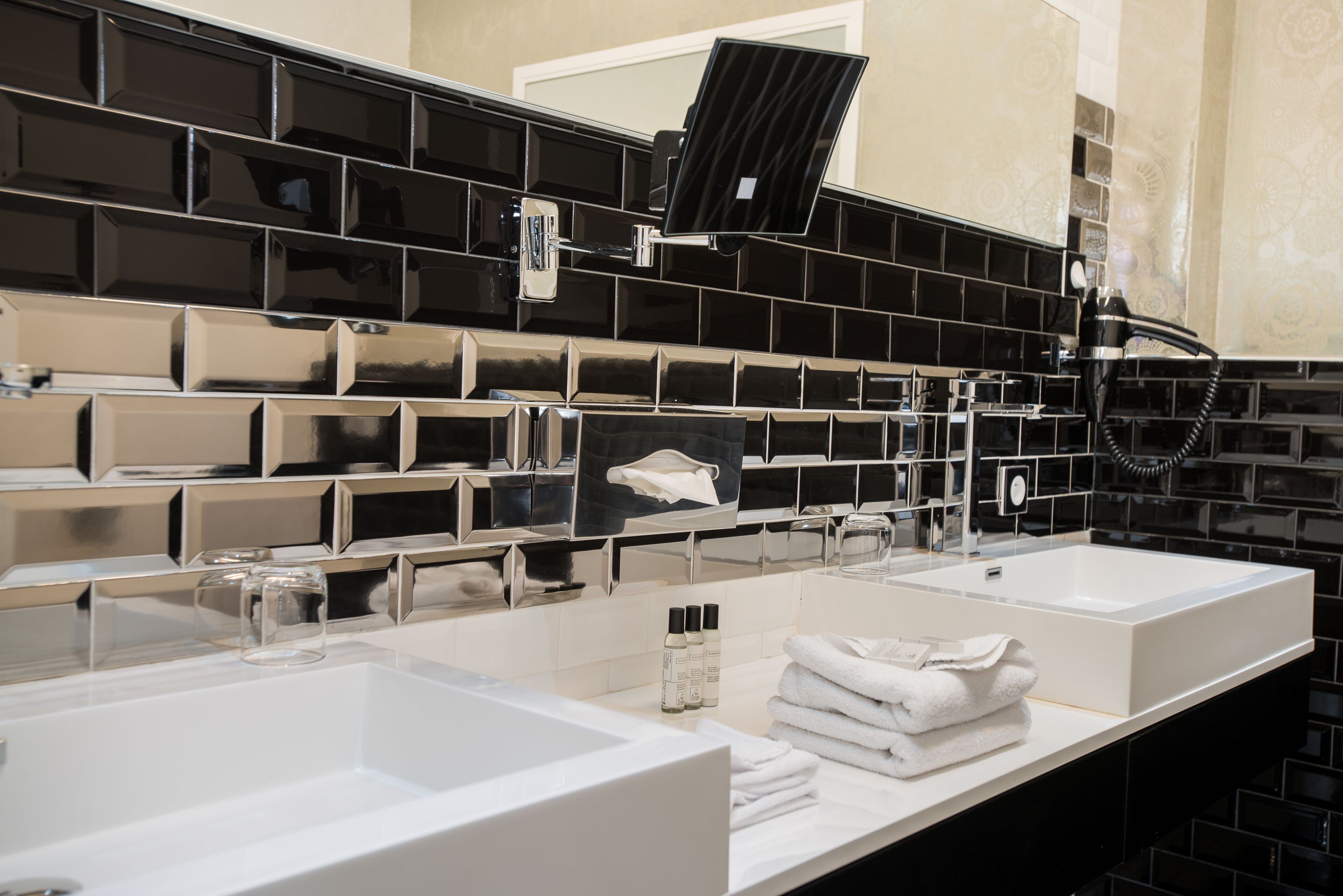 A modern bathroom with two sinks, a mirror, and a black-tiled backsplash.