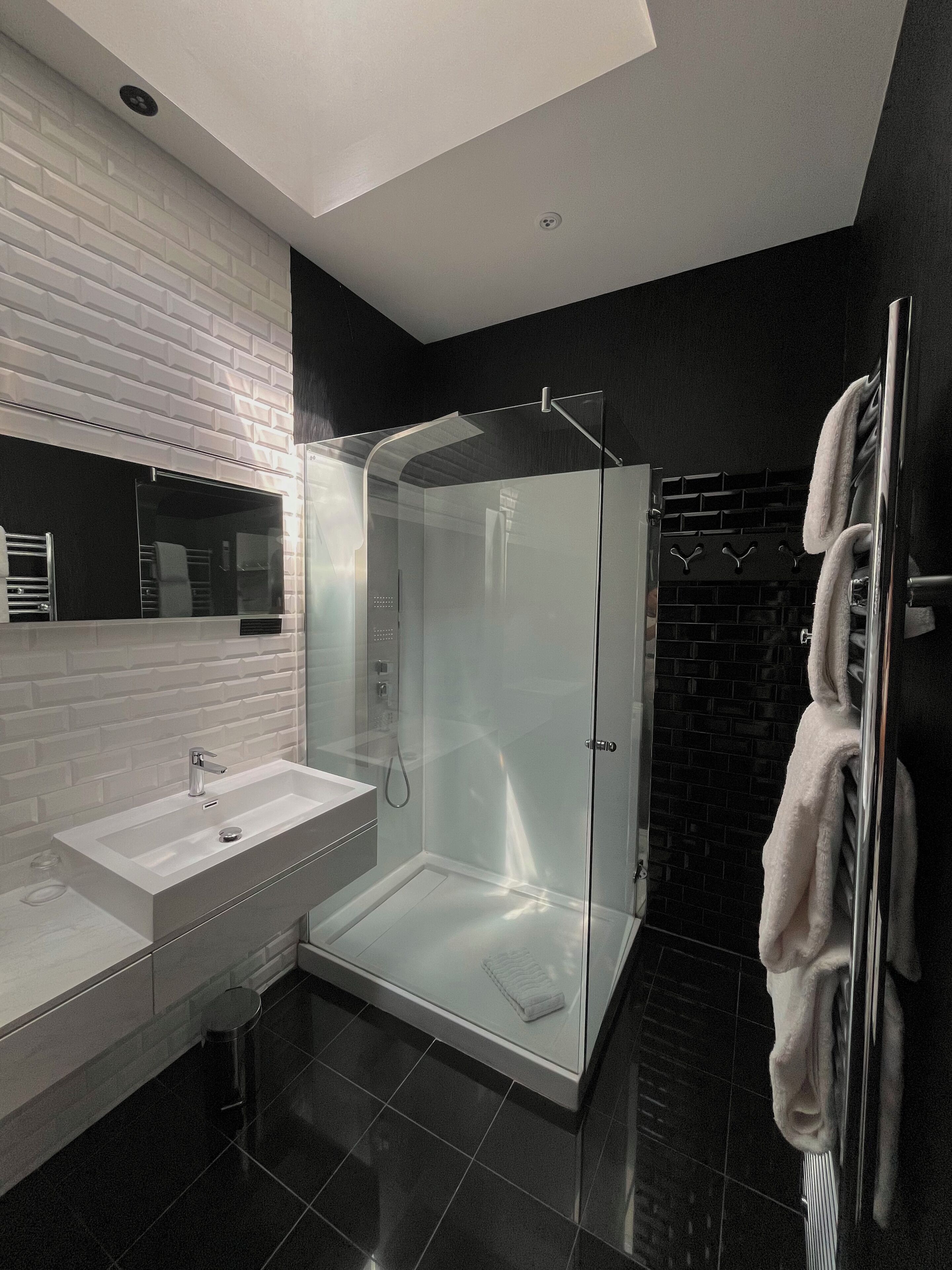 Une salle de bain moderne avec une douche à parois de verre, un lavabo blanc et un sol carrelé de noir.