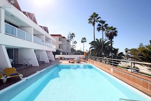 Un espace piscine avec des chaises longues et vue sur l’océan.