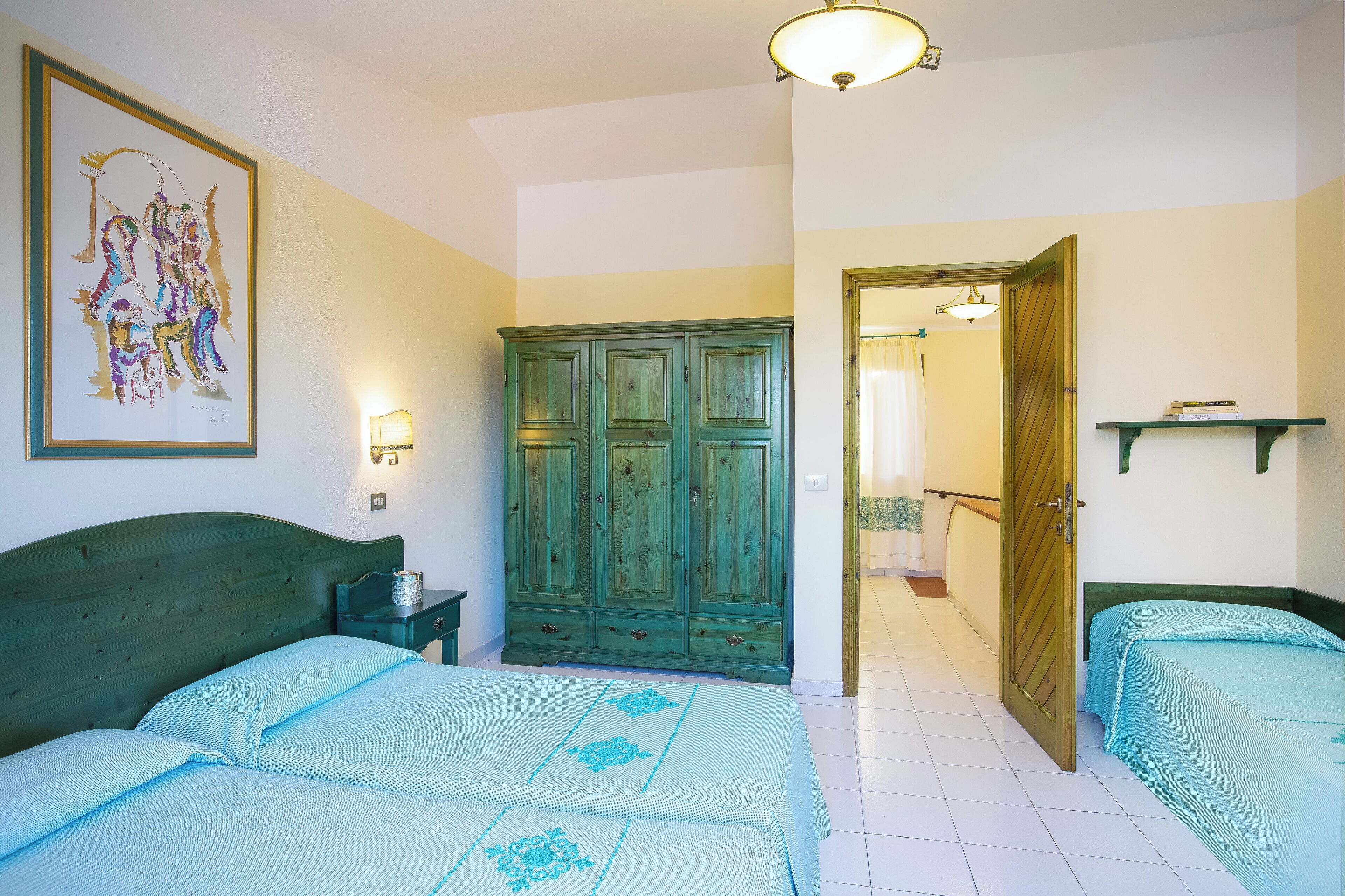 A room with two beds, a wardrobe, a painting, and a light fixture.