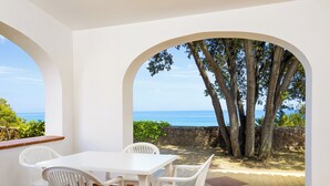 A patio with a white table and chairs, a stone wall, and a view of the sea through an archway. - Alba Dorata Resort (Orosei)