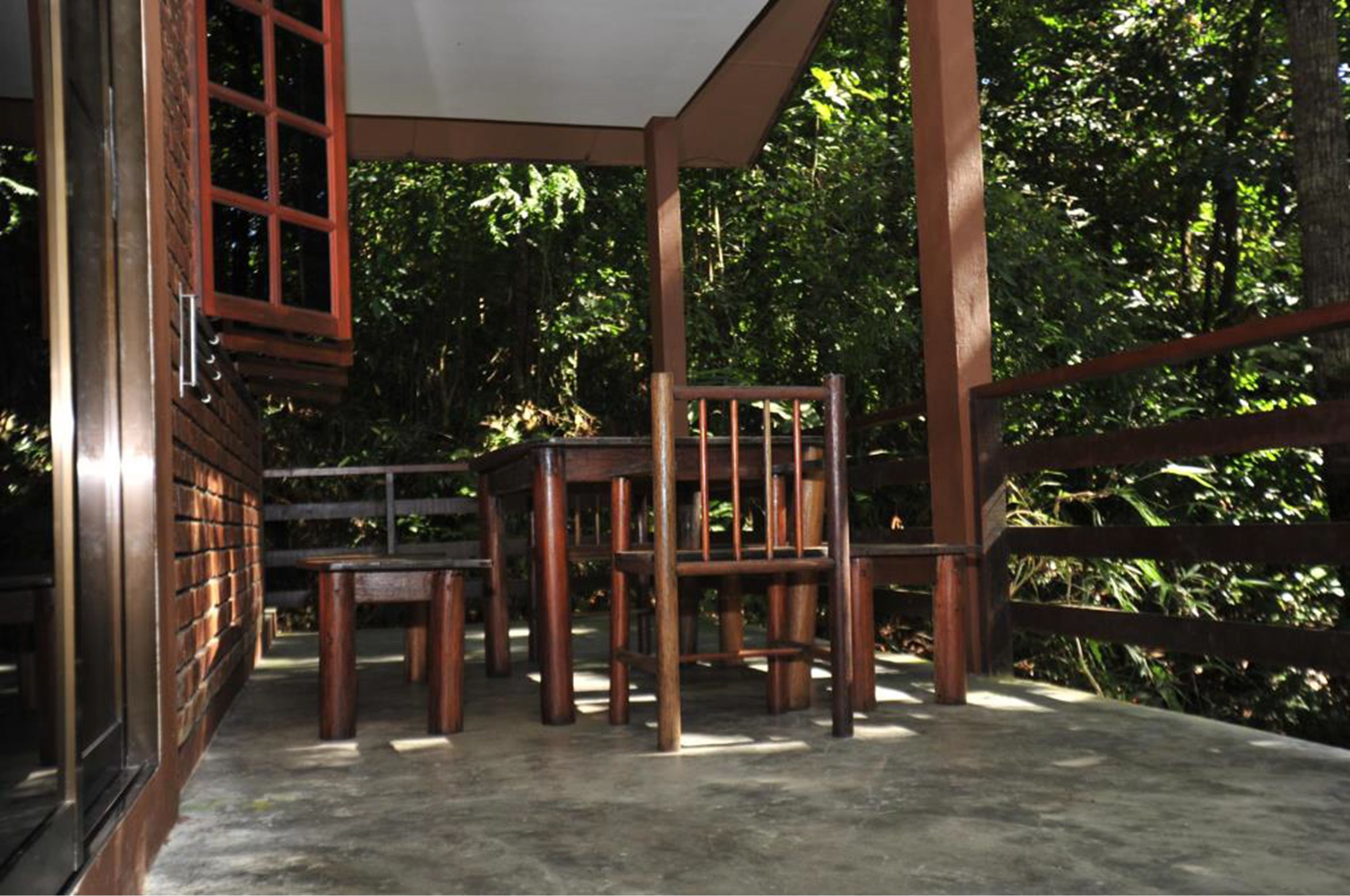 An outdoor wooden deck with a table and chairs, surrounded by lush greenery.
