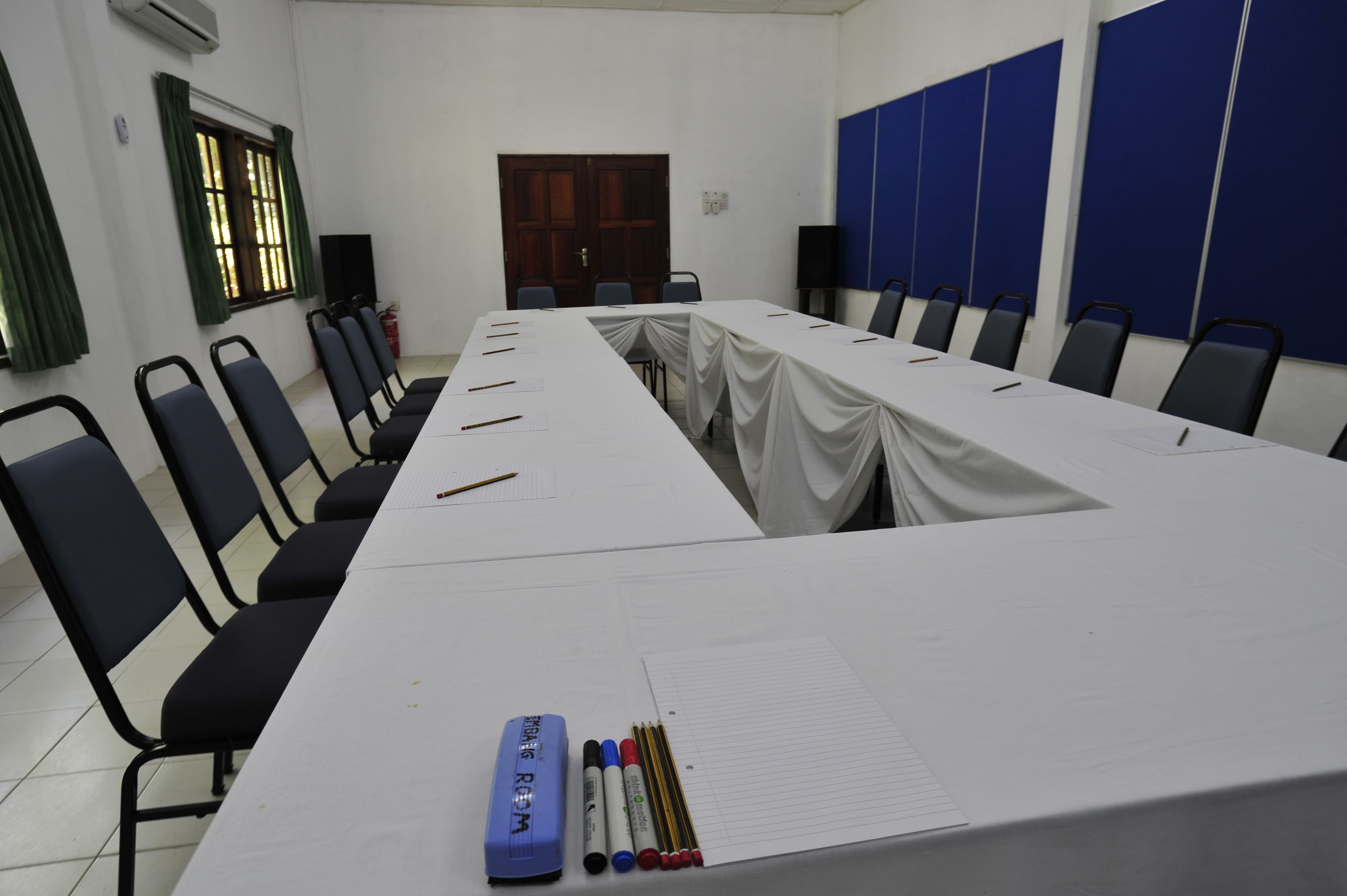 A conference room with a long table, chairs, and writing materials.