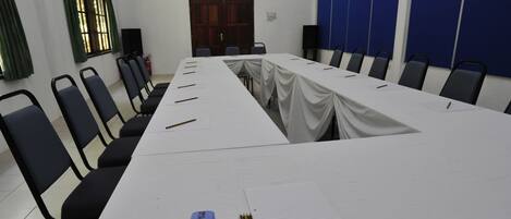 Un salón de conferencias con una larga mesa, sillas y material de escritura.