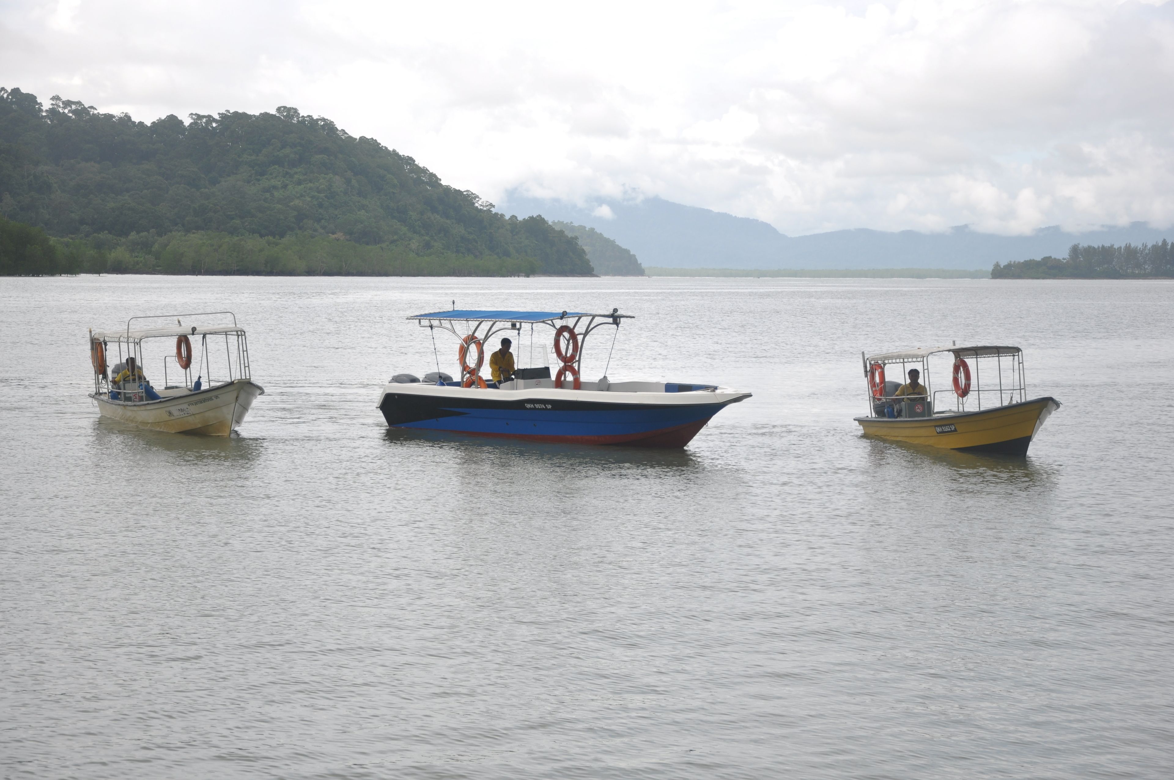 Three boats on a calm lake with a forested island in the background.